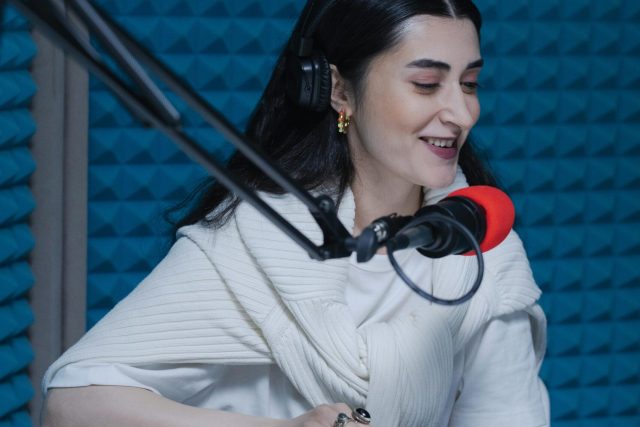 Smiling woman podcaster recording in a soundproof studio with headphones and microphone.